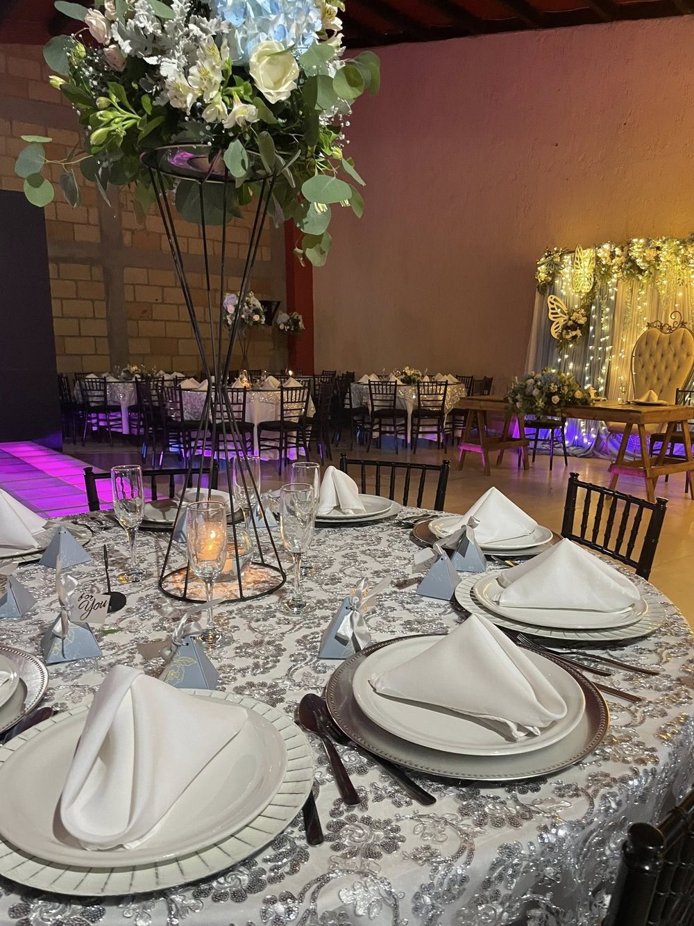Mesa montada con mantelería plateada y centro floral alto en El Realejo